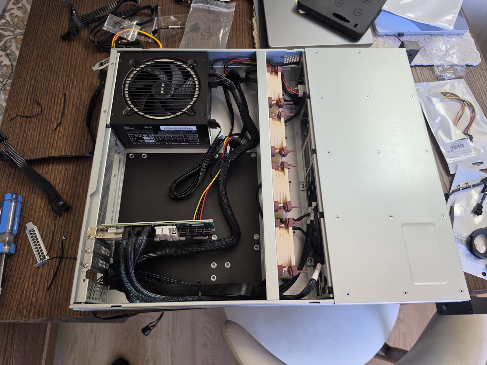 The disk shelf mid-build on the kitchen table: power supply and fan wall mounted, host bus adapter cabled to the drive backplane, bays still waiting for their drives.
